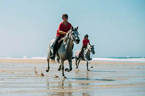Twee mensen rijden paard op het strand aan de Atlantische Kust van Frankrijk.