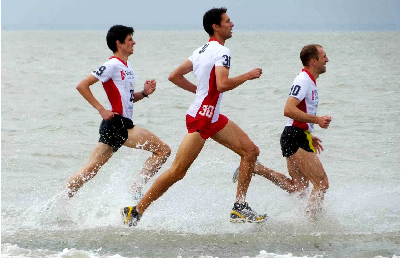 Drie mannen rennen door de zee tijdens een hardloopwedstrijd in Les Foulees du Gois.